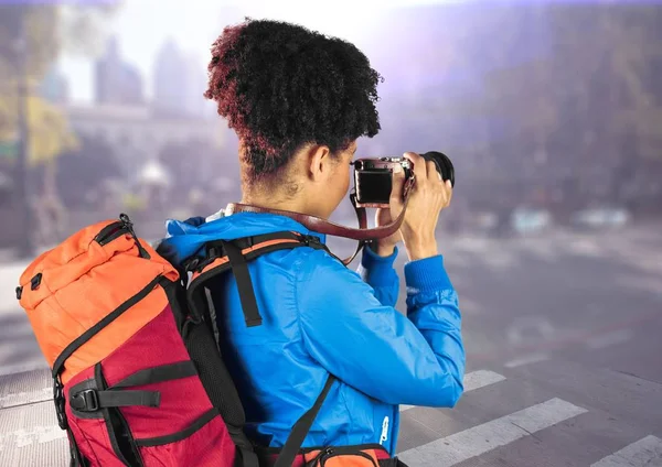 Millennial backpacker with camera against blurry street with flare — Stock Photo, Image