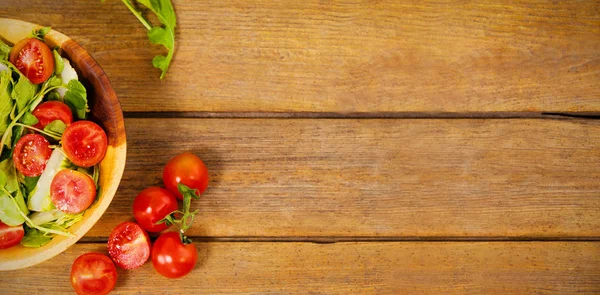 Свежий салат в миске с помидорами на деревянном столе — стоковое фото