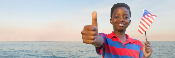 Jongen met Amerikaanse vlag geven duimen tegen water en avondlucht — Stockfoto