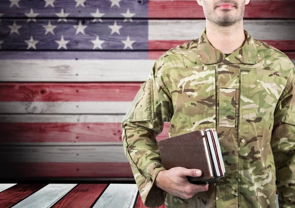 Soldado sosteniendo libros frente a la bandera americana — Foto de Stock