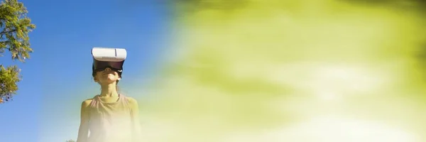Низький кут дівчини з гарнітурою віртуальної реальності на фоні неба з розмитим зеленим переходом — стокове фото