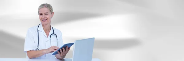 Doctor at computer with tablet against white blurred abstract background — Stock Photo, Image