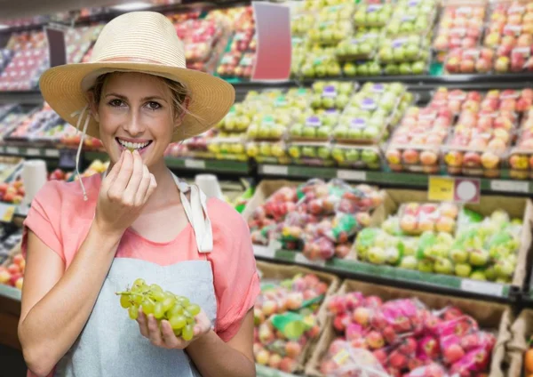 Mujer comiendo uvas contra pasillo borroso de comestibles — Foto de Stock