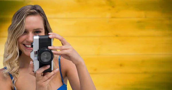 Close up of millennial woman with camera against blurry yellow wood panel — Stock Photo, Image