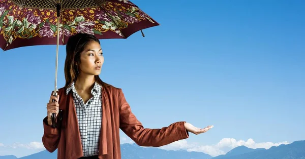 Tusenåriga kvinna med mönstrat paraply och hand ut mot bergstopparna och sky — Stockfoto