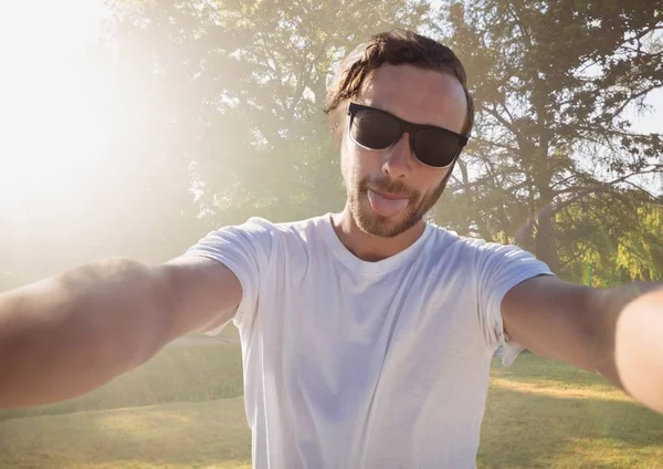 Millennial homem tomando selfie e furar a língua no parque embaçado com flare — Fotografia de Stock
