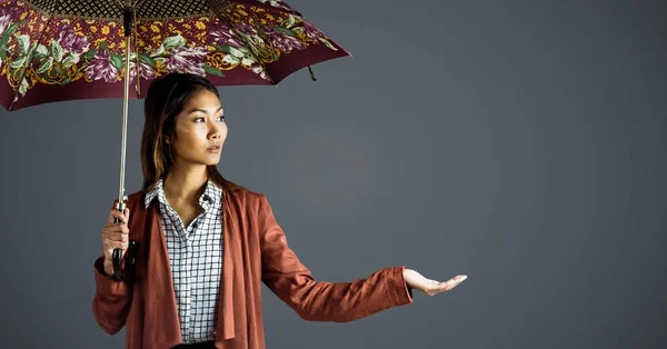 Tusenåriga kvinna med mönstrat paraply och hand ut mot grå bakgrund — Stockfoto