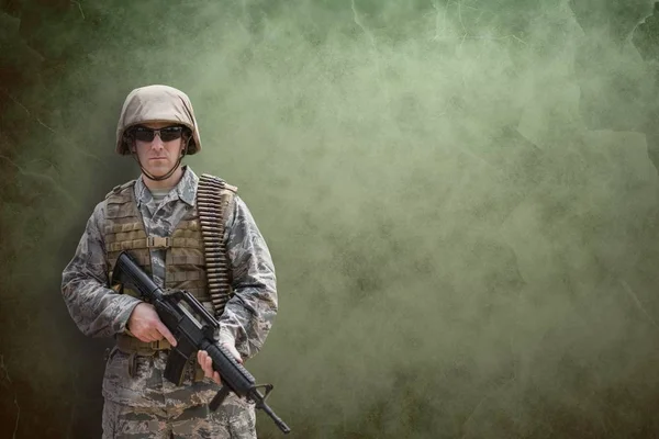 Soldado segurando uma arma contra fundo verde — Fotografia de Stock