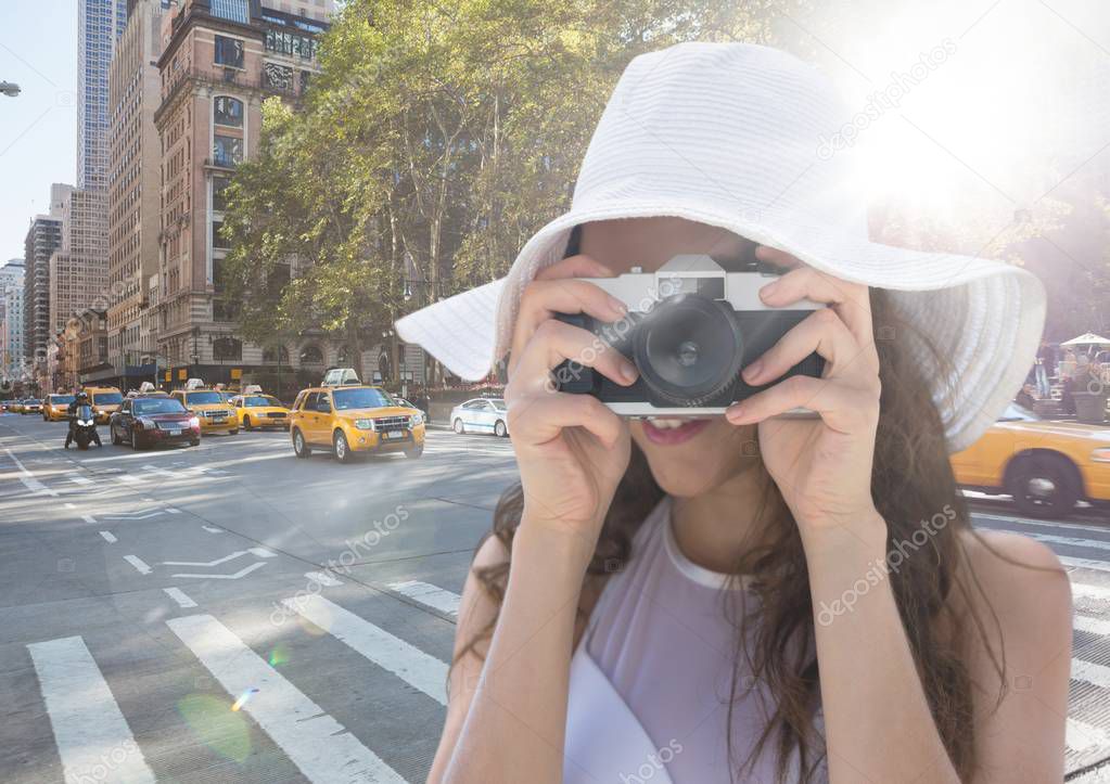 Close up of millennial woman in summer hat with camera against street with flare