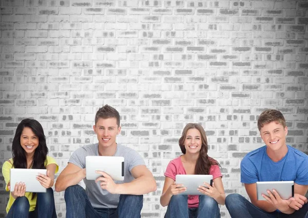 Group of students on devices in front of grey brick background — Stock Photo, Image