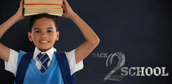 Leende skolpojke bär böcker på huvud — Stockfoto