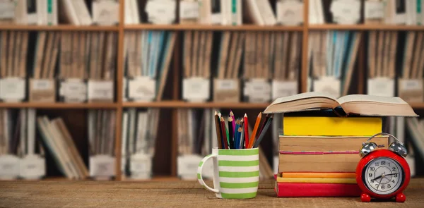 Imagem composta de pilha de livros por caneca com lápis coloridos e despertador na mesa de madeira — Fotografia de Stock