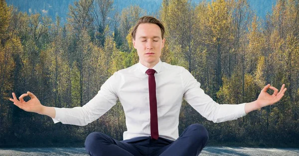 Business man meditating against trees — Stock Photo, Image