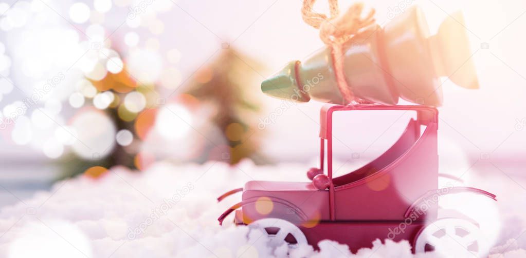 Toy car carrying christmas tree on fake snow during christmas time