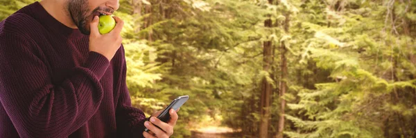 Man met behulp van de telefoon tijdens het eten apple — Stockfoto