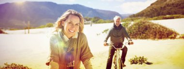 Carefree couple going on a bike ride on the beach on a bright but cool day clipart