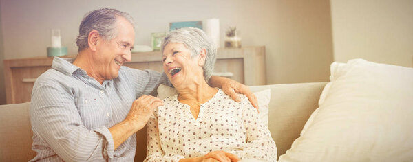 Romantic senior couple laughing while sitting on sofa at home