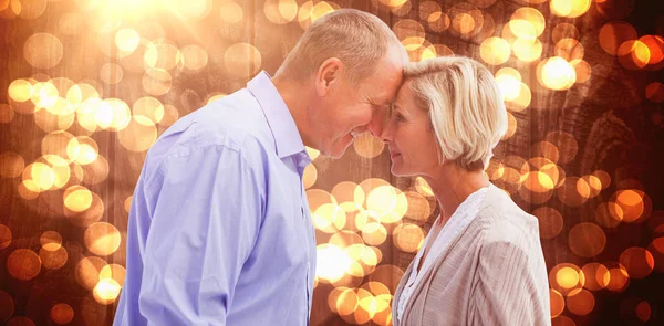 Happy mature couple facing each other against blurred orange light