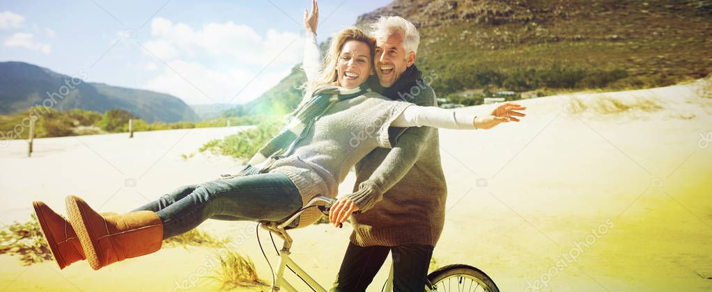 Carefree couple going on a bike ride on the beach on a bright but cool day