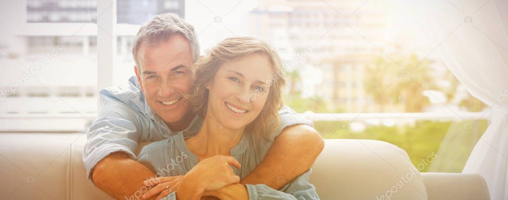 Content man hugging his wife on the couch smiling at camera at home in the living room
