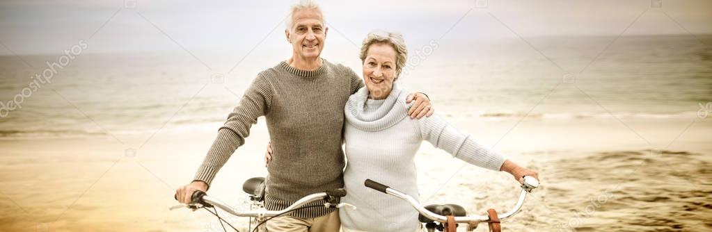 Portrait of happy senior couple with their bike on the beach