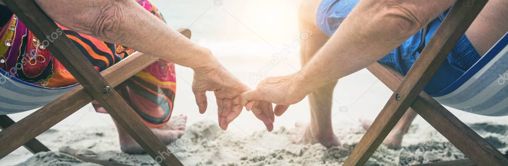 Rear view of senior couple sitting on deckchairs and holding hands while relaxing on the beach