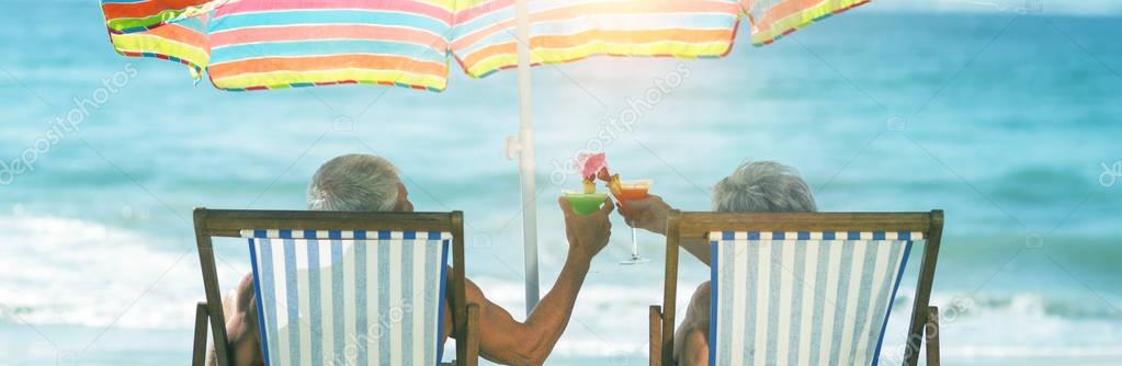 Cute mature couple lying on deckchairs at beach