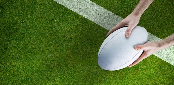 A rugby player posing a rugby ball against pitch with line