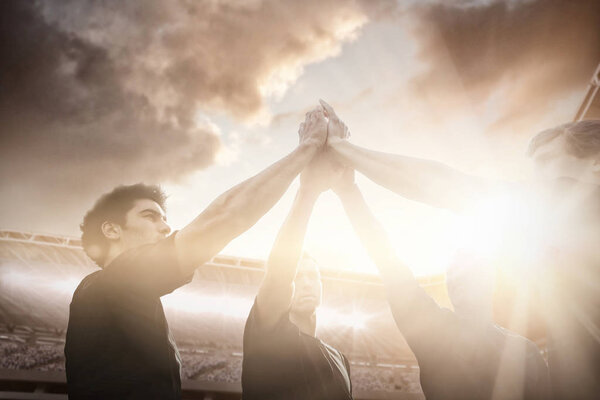 Композитный имидж спортивной арены с болельщиком против регбистов, стоящих вместе перед матчем
