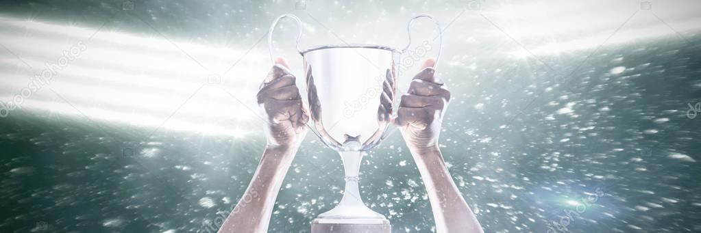 Cropped hand of athlete holding trophy against black background