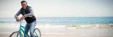 Digital composite of handsome man on a bike ride against scenic view of beach clipart