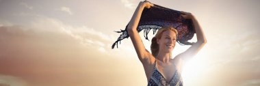 Kadın holding eşarp hava plaj manzarasına karşı günbatımı sırasında gülümseyen