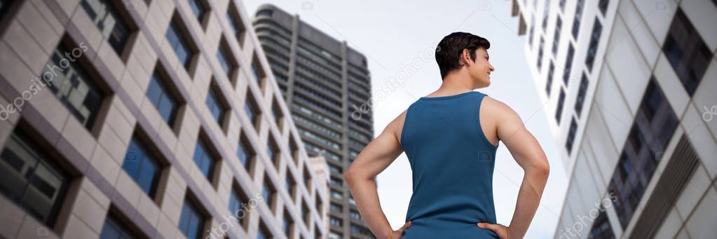 Smiling young man with hands on hip standing over white background against low angle view of office towers