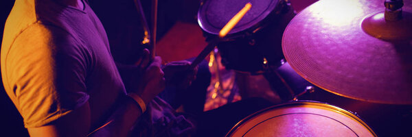 Высокий угол зрения исполнителя, играющего на барабане в освещенном ночном клубе
