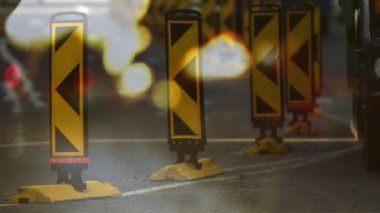 Şehir caddesinde yol trafiği ve ön planda bulanık ışıklarla yürüyen insanların canlandırması