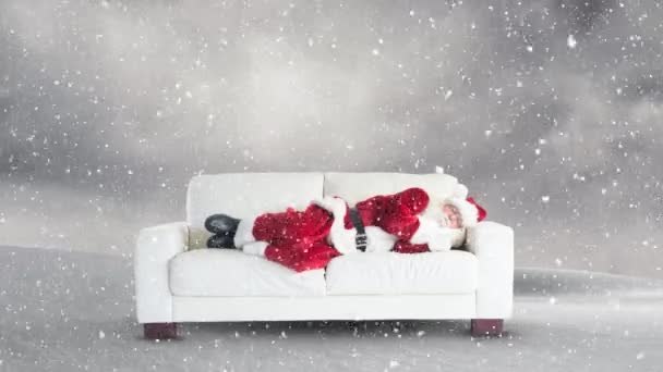 雪の降る冬の風景のアニメーションと背景に白いソファに横たわって疲れたサンタクロース — ストック動画