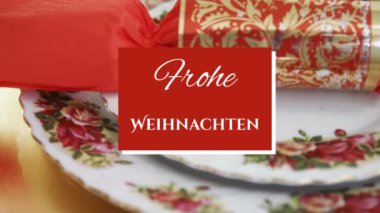 Kırmızı meydanda beyaz yazılı Frohe Weihnachten kelimelerinin animasyonu. Arka planda Noel krakeri ve çam kozalağı var.