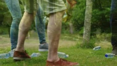 Bir grup insanın plastik şişeleri toplayıp ön planda hareket eden kırsal bölgeleri olan siyah bir çöp torbasına koyması.