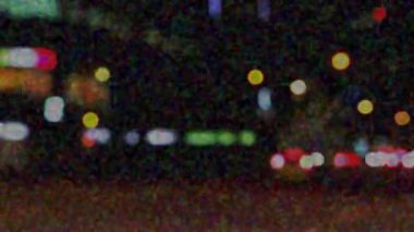 Şehirdeki gece trafiğinin animasyonu. Ön planda bulanık şehir ışıkları ve gürültü tahılları var.