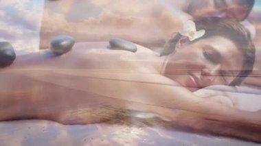 Genç bir çiftin ön planda hareket eden denizle sıcak taş masajı yaptırdığı animasyon.