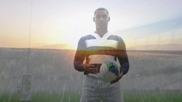 一名非裔美国男子橄榄球运动员举着球 凝视着前方下着雨的体育场的动画 — 图库视频影像