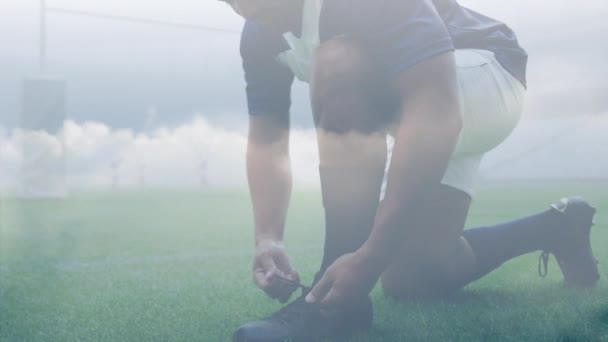 橄榄球运动员和他的队友将鞋带绑在橄榄球球场上的动画和后面的烟云 — 图库视频影像
