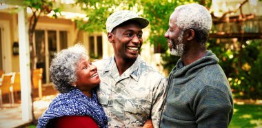 Front view of a young adult African American male soldier in the garden outside his home embracing and smiling with his parents
