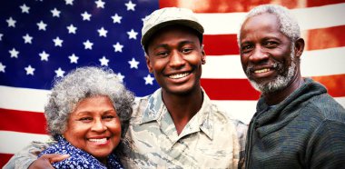 Genç bir Afro-Amerikan erkek askerin portresi. Ailesiyle kucaklaşıyor. Hepsi Amerikan bayrağı önünde kameraya gülümsüyor.