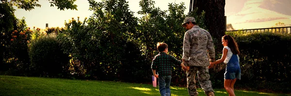 一个年轻的成年男女混血儿手牵手 牵着他的小儿子和女儿 他的儿子举着一面美国国旗 在自家花园外的后视镜 — 图库照片