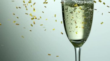 Beyaz arka planda yeni yıl kutlamaları sırasında altın konfetilerin döküldüğü dolu bir şampanya kadehinin animasyonu