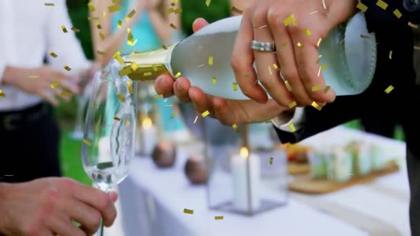シャンパンボトルを持っている人のアニメーションと黄金のコンフェッティが落ちるガラスにシャンパンを注ぐとパーティーでバックグラウンドで祝うと拍手の人々のグループ — ストック動画