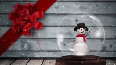İçinde kardan adam olan Noel kar küresinin animasyonu, kırmızı kurdele ve arka planda gri ahşap tahtalar ile düşen kar.