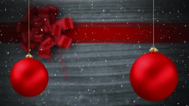 雪のアニメーションは グレーの背景に弓と2つの赤いボールクリスマスの装飾と赤いリボンで落ちる — ストック動画