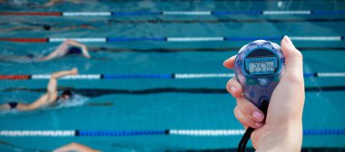 Havuzda yüzen yüzücülerin performansını ölçmek için kronometre tutan bir kadının yakın çekimi.
